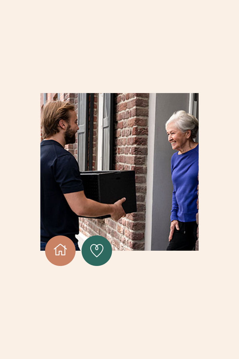 lachender Mann übergibt eine Isolierbox an ältere Damen an der Haustür