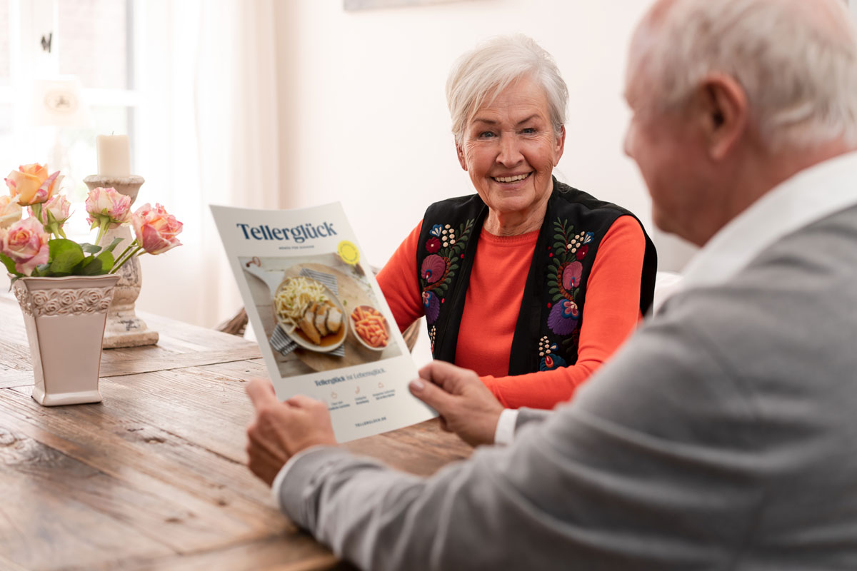 Älteres Paar sitzt am Tisch und schaut gemeinsam in den Tellerglück Katalog
