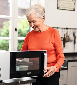 Eine Seniorin legt ein Menü in eine Mikrowelle