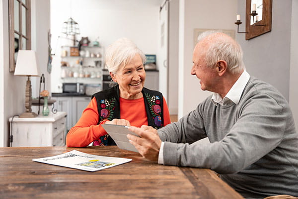 Älteres Paar sitzt am Tisch und schaut gemeinsam auf ein Tablet