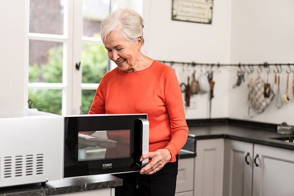 Eine ältere Dame stellt ein Tiefkühlgericht in ihre Mikrowelle