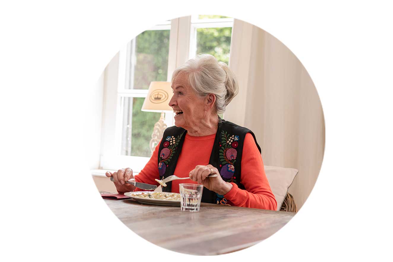 lachende ältere Frau am Tisch beim Essen