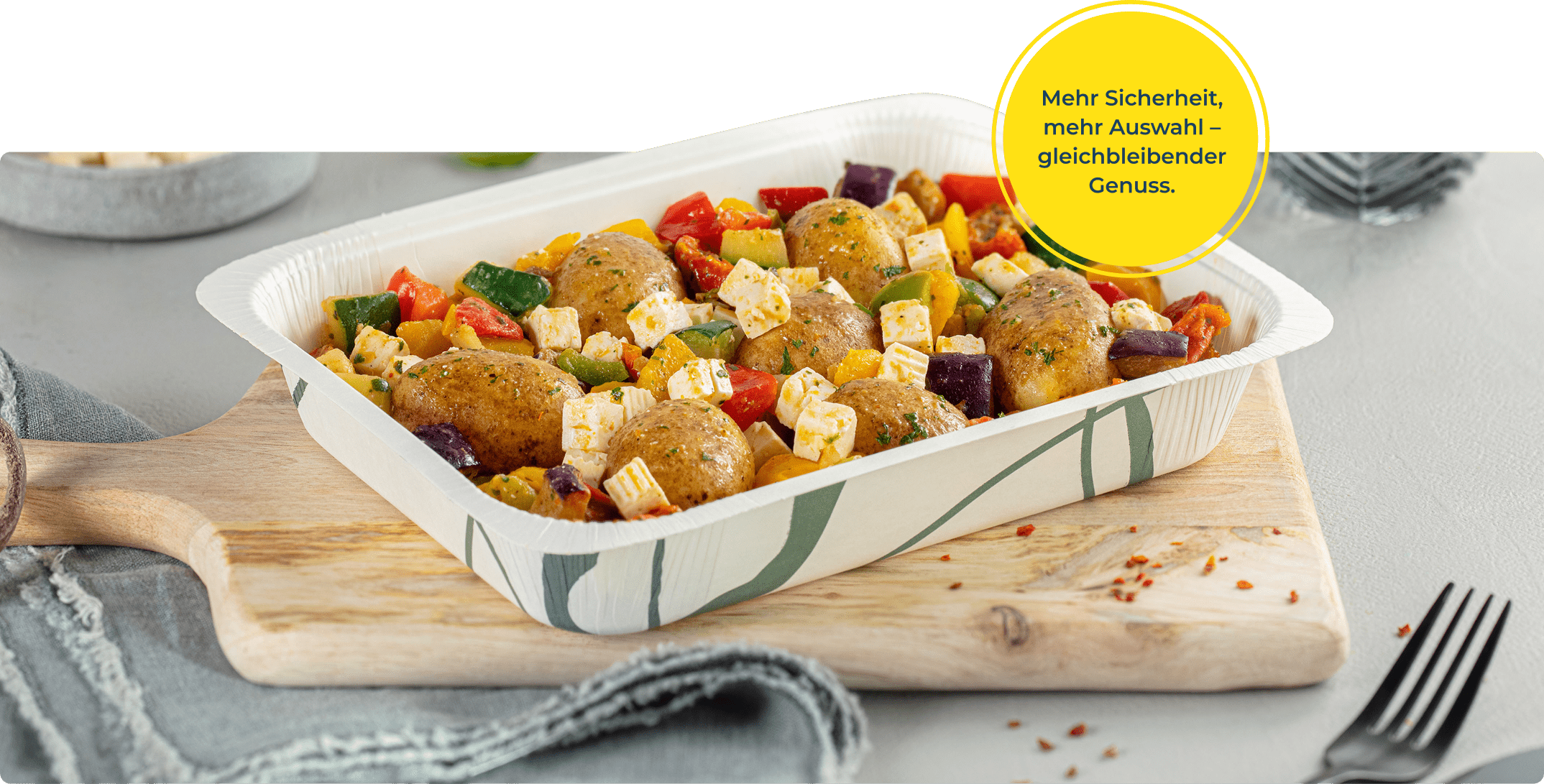 Es ist zentral eine Menüschale des neuen Sortiments zu erkennen. In der Menüschale ist ein mediterranes Kartoffel-Gericht. Oben rechts ist ein gelber Kreis eingeblendet, in dem steht: "Mehr Sicherheit, mehr Auswahl - gleichbleibender Genuss.