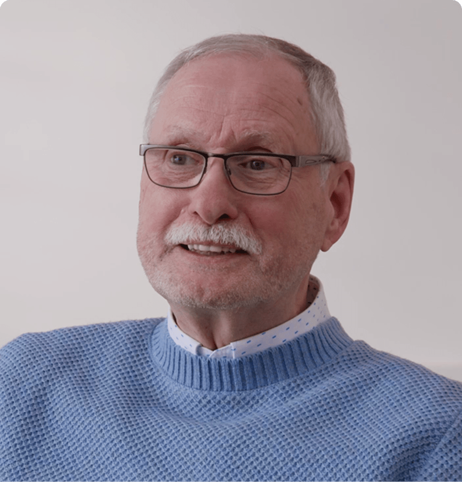 Person in einem hellblauen Strickpullover sitzt vor hellem Hintergrund.