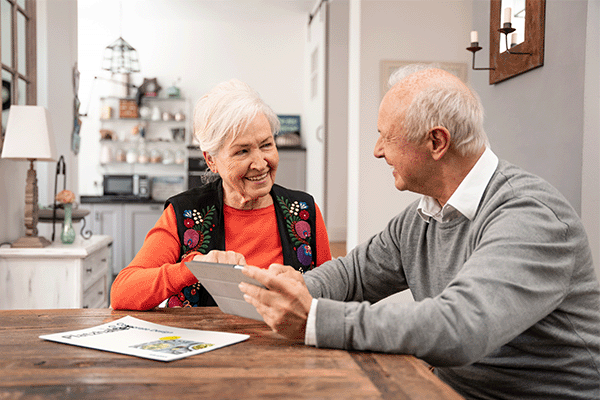 Älteres Paar sitzt am Tisch und schaut gemeinsam auf ein Tablet