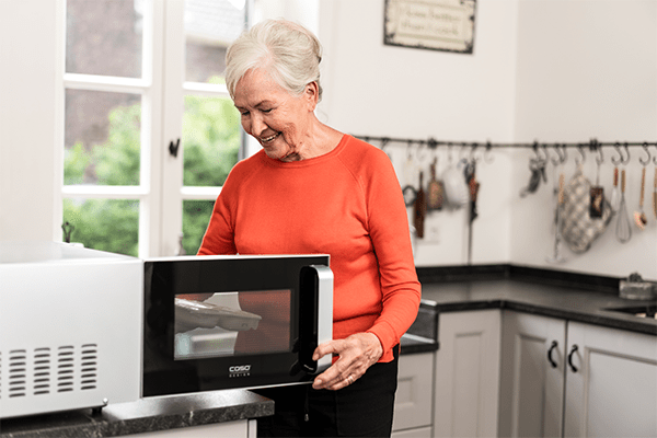 Eine ältere Dame stellt ein Tiefkühlgericht in ihre Mikrowelle