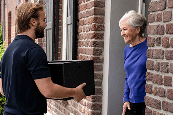lachender Mann übergibt eine Isolierbox an ältere Damen an der Haustür