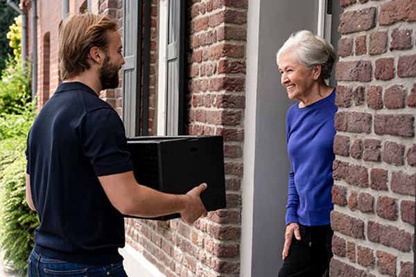 lachender Mann übergibt eine Isolierbox an ältere Damen an der Haustür