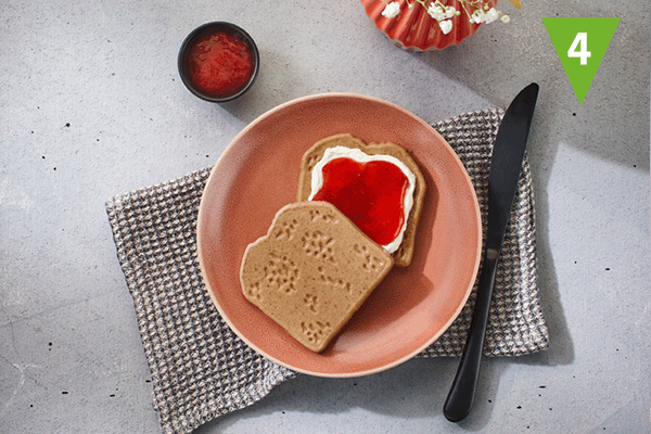 Pürierte Brotzeitschnitte in Form von Brotscheiben, eine davon bestrichen mit Quark und Erdbeermarmelade